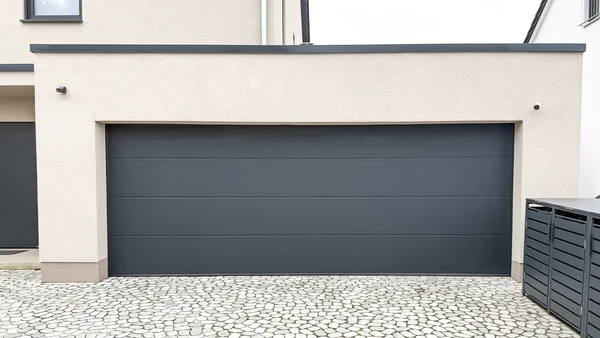 Extérieur résidentiel moderne avec porte de garage sectionnelle grise à panneaux horizontaux, intégrée dans façade blanche contemporaine